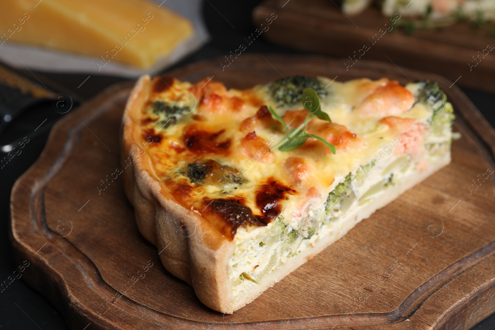 Photo of Piece of delicious homemade quiche with salmon and broccoli on wooden board, closeup