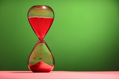 Photo of Hourglass with red flowing sand on color background. Space for text