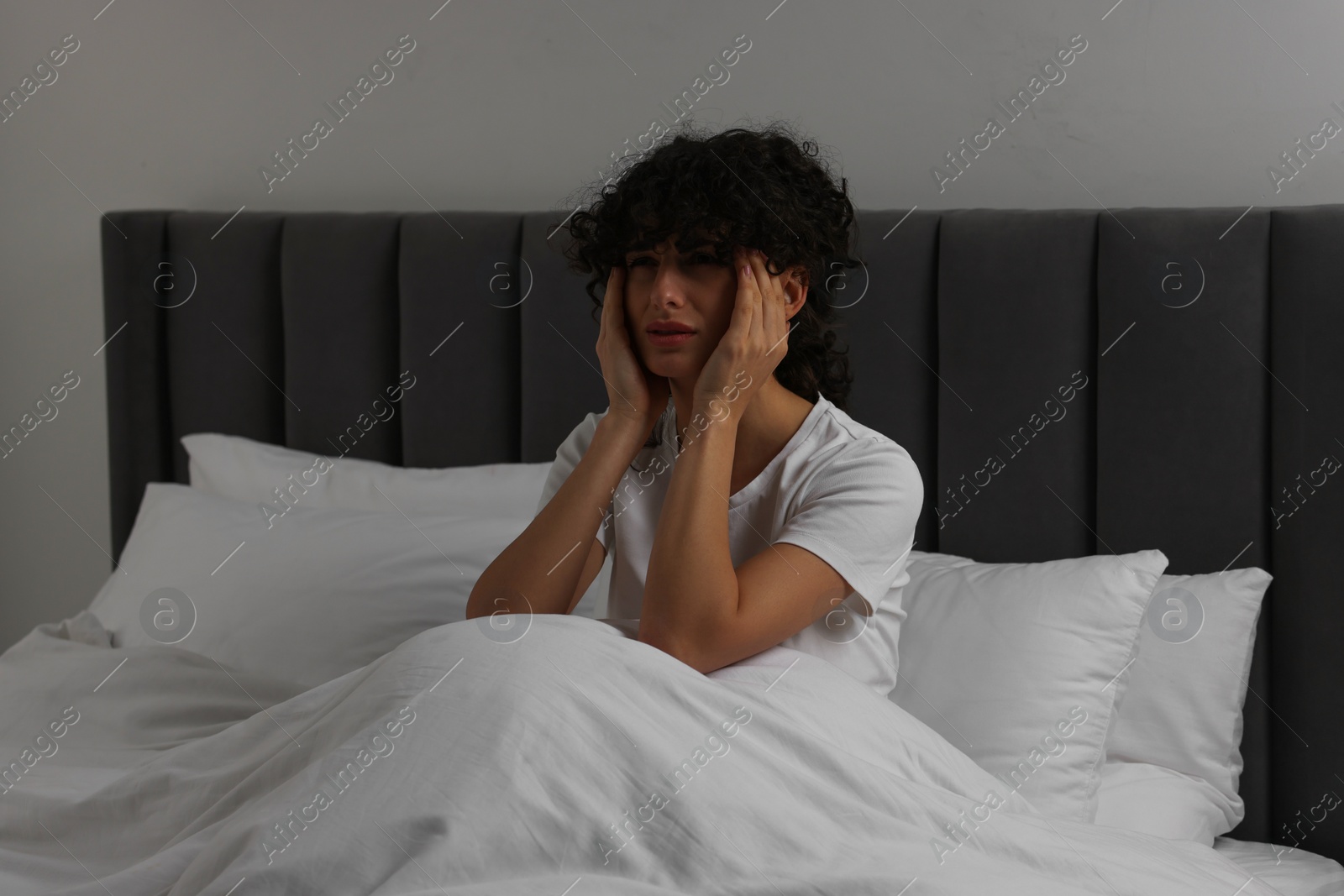 Photo of Young woman suffering from headache in bed at night