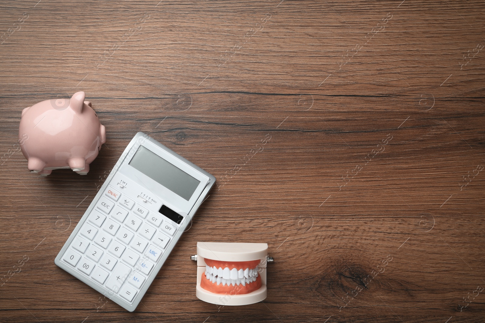 Photo of Educational dental typodont model, piggy bank and calculator on wooden table, flat lay with space for text. Expensive treatment