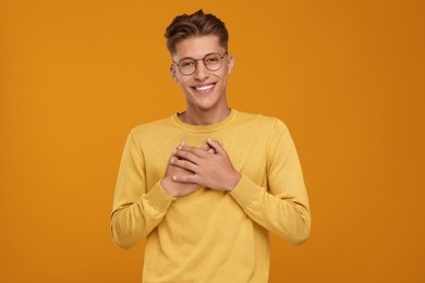 Photo of Thank you gesture. Happy grateful man with hands on chest against orange background