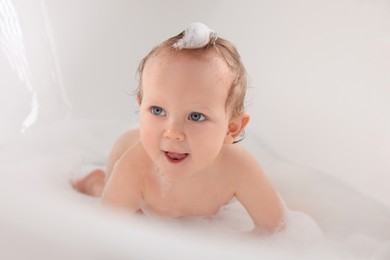 Photo of Cute little baby taking foamy bath at home