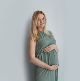 Young pregnant woman touching belly on light background