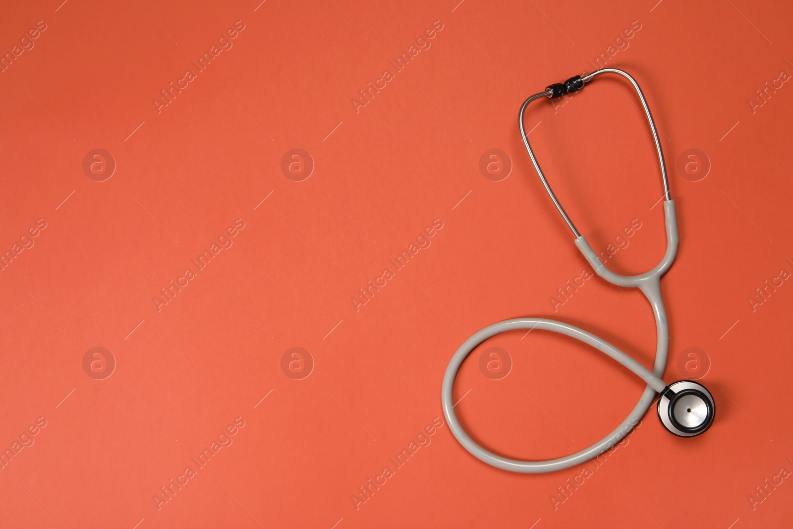 Photo of Stethoscope on crimson background, top view. Space for text