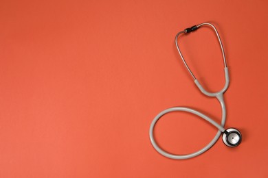 Photo of Stethoscope on crimson background, top view. Space for text