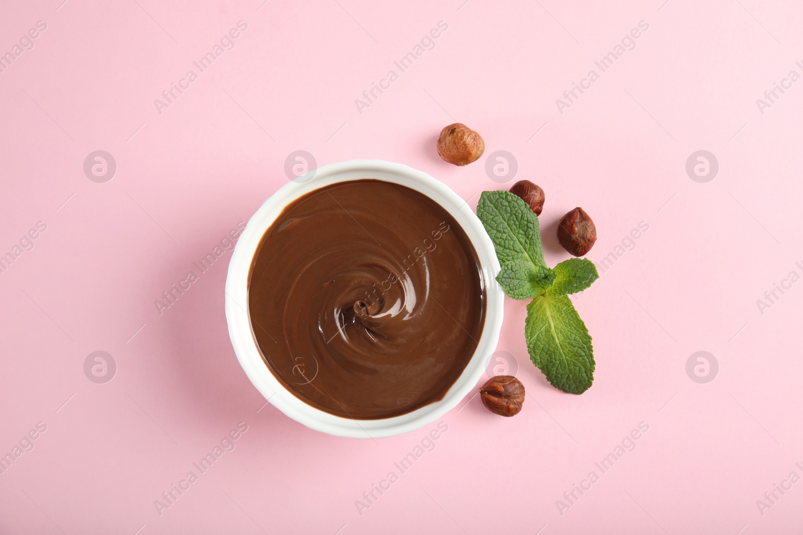 Photo of Ceramic bowl with sweet chocolate cream, hazelnuts and mint on color background, top view