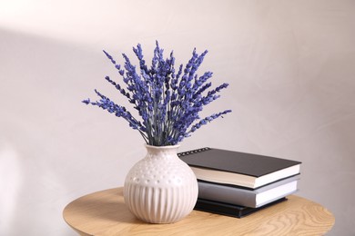 Bouquet of beautiful preserved lavender flowers and notebooks on wooden table near beige wall