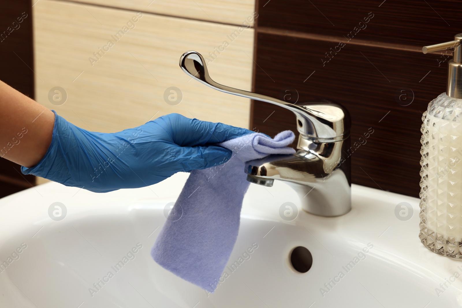 Photo of Woman in gloves cleaning faucet of bathroom sink with rag, closeup