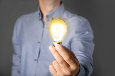 Image of Glow up your ideas. Man holding light bulb on grey background, closeup