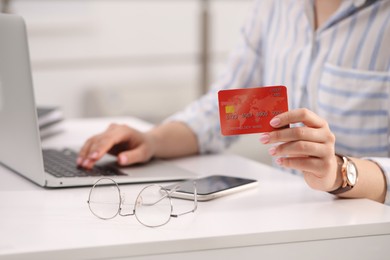 Woman with credit card using laptop for online shopping at white table, closeup