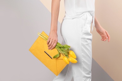 Stylish woman with clutch and spring flowers against color background, closeup