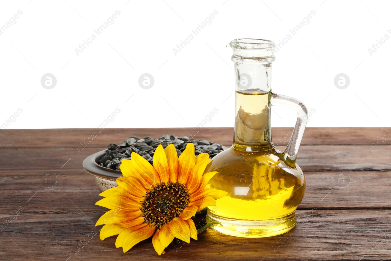 Photo of Sunflower, jug of oil and seeds on wooden table against white background