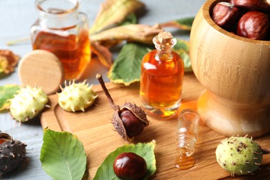 Photo of Horse chestnuts, leaves and bottles of tincture on grey wooden table, closeup