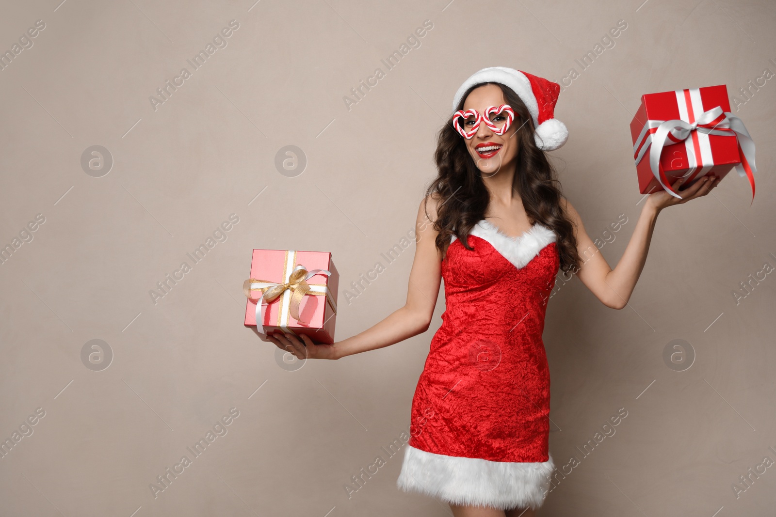 Photo of Beautiful woman in Christmas costume with gift boxes on beige background