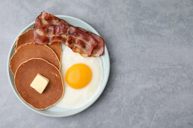 Photo of Tasty pancakes with fried egg and bacon on grey table, top view. Space for text