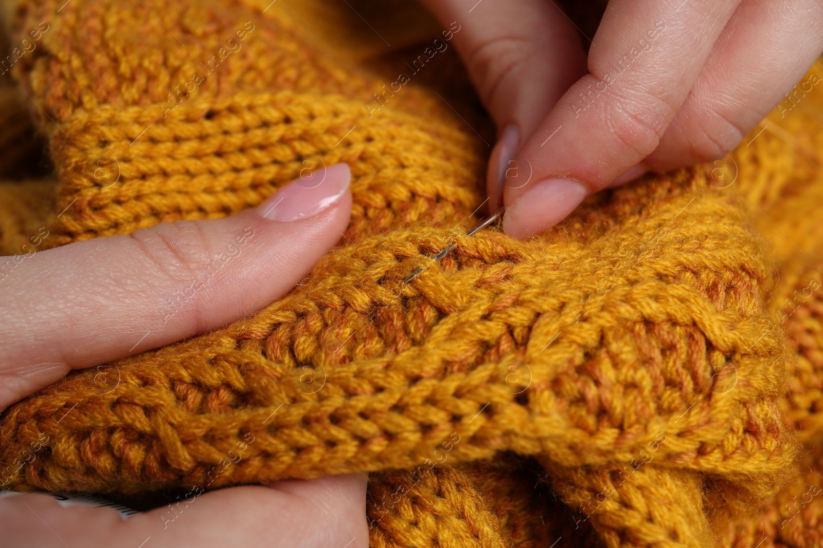 Photo of Woman sewing sweater with needle, closeup view