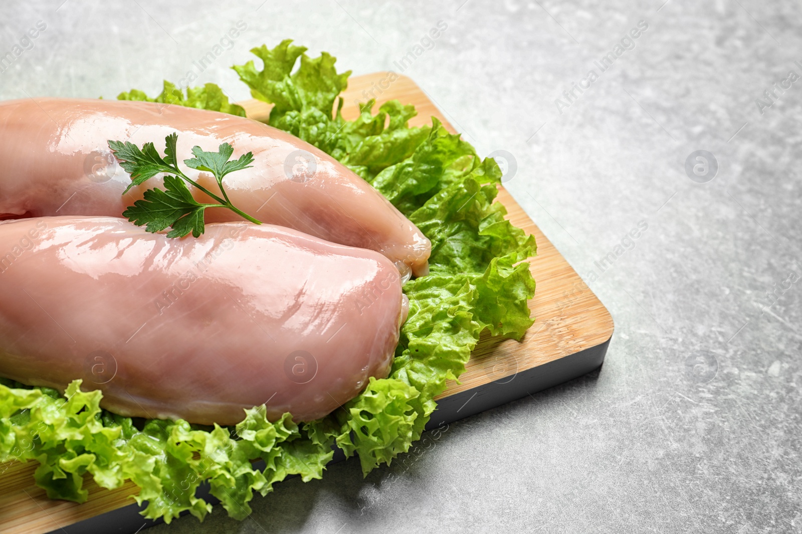 Photo of Wooden board with raw chicken breasts and lettuce on grey background