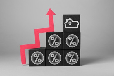 Mortgage rate rising illustrated by upward arrow, black cubes with percent signs and house icon on gray background