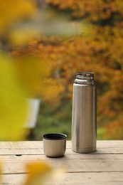 Photo of Metallic thermos and cup lid on wooden table outdoors