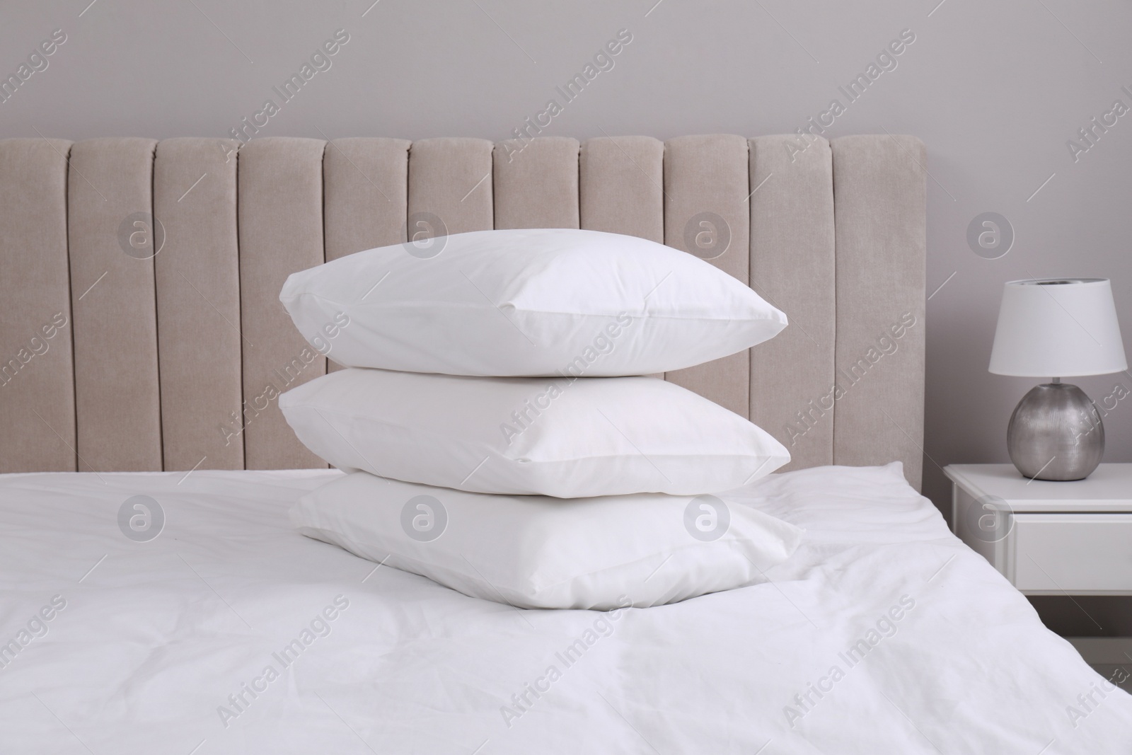 Photo of White soft pillows on bed and lamp in room