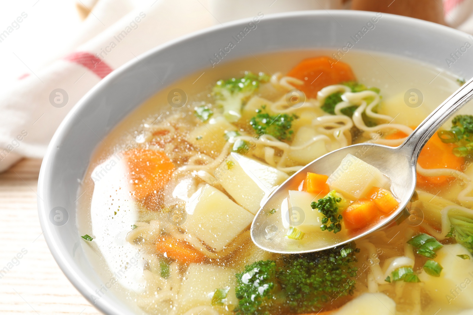 Photo of Spoon of fresh homemade vegetable soup over full bowl on table, closeup