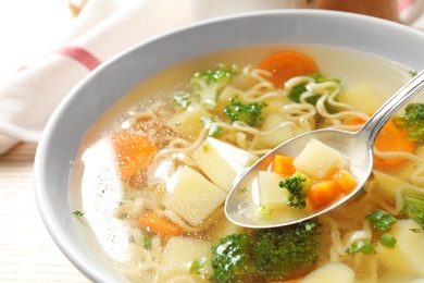 Photo of Spoon of fresh homemade vegetable soup over full bowl on table, closeup