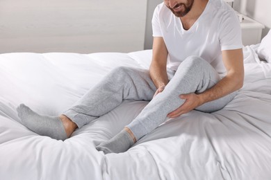 Photo of Man suffering from leg pain on bed at home, closeup