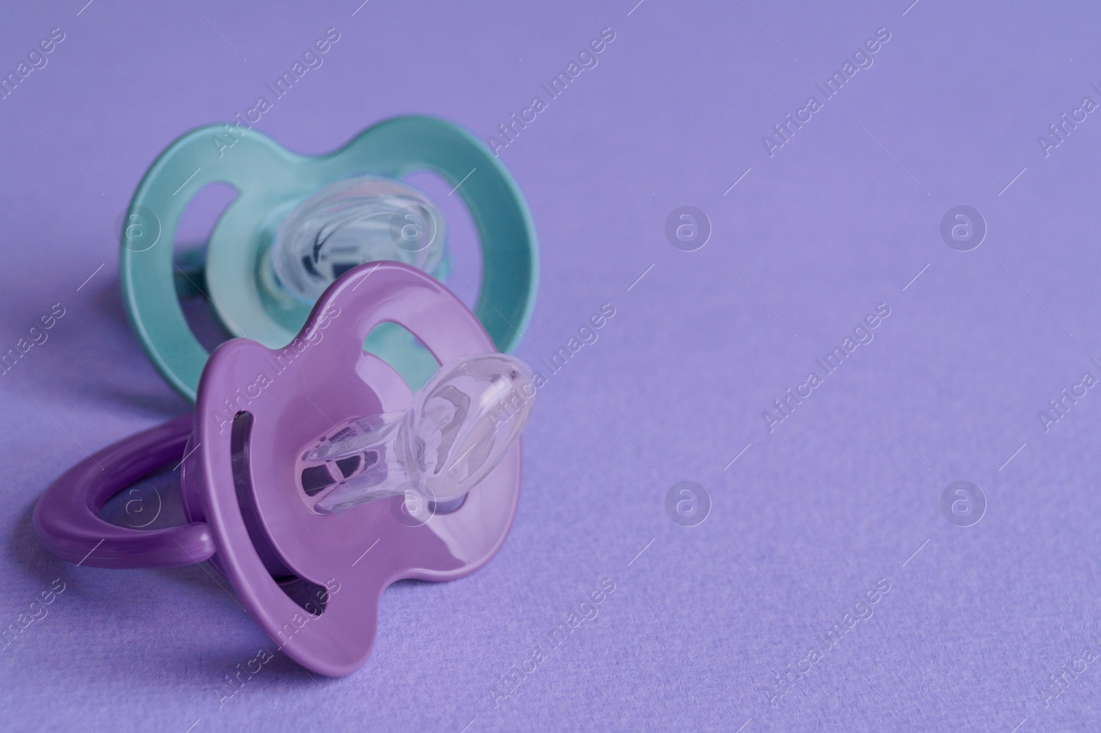 Photo of New baby pacifiers on purple background, closeup. Space for text