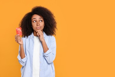 Photo of Confused woman with credit card on orange background, space for text. Debt problem