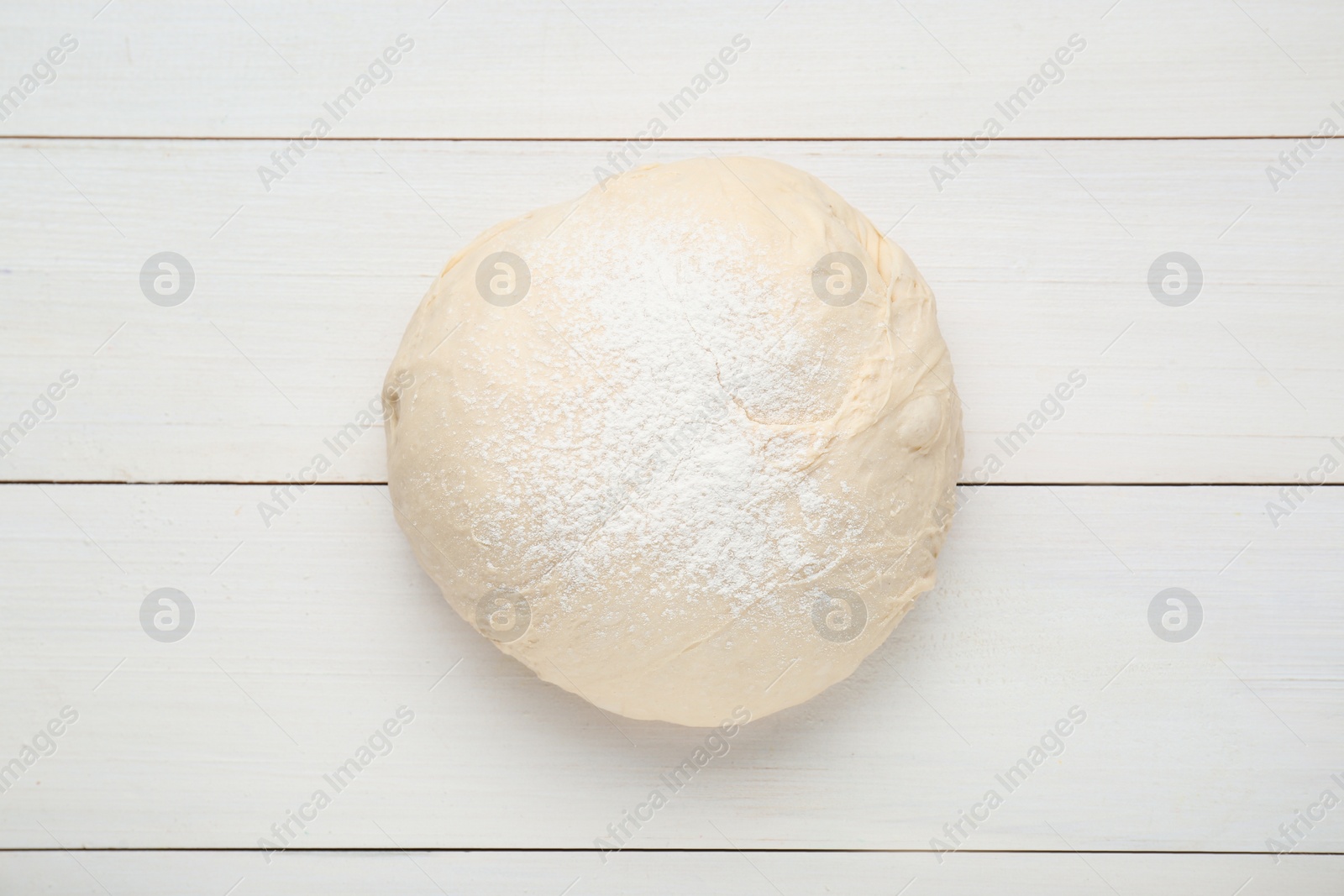 Photo of Fresh yeast dough with flour on white wooden table, top view