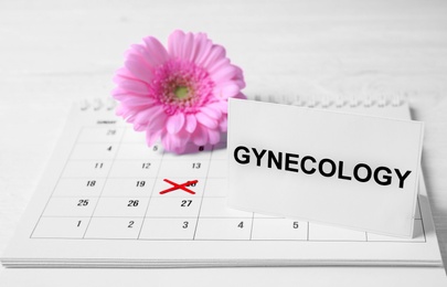 Photo of Card with word Gynecology, calendar and flower on table