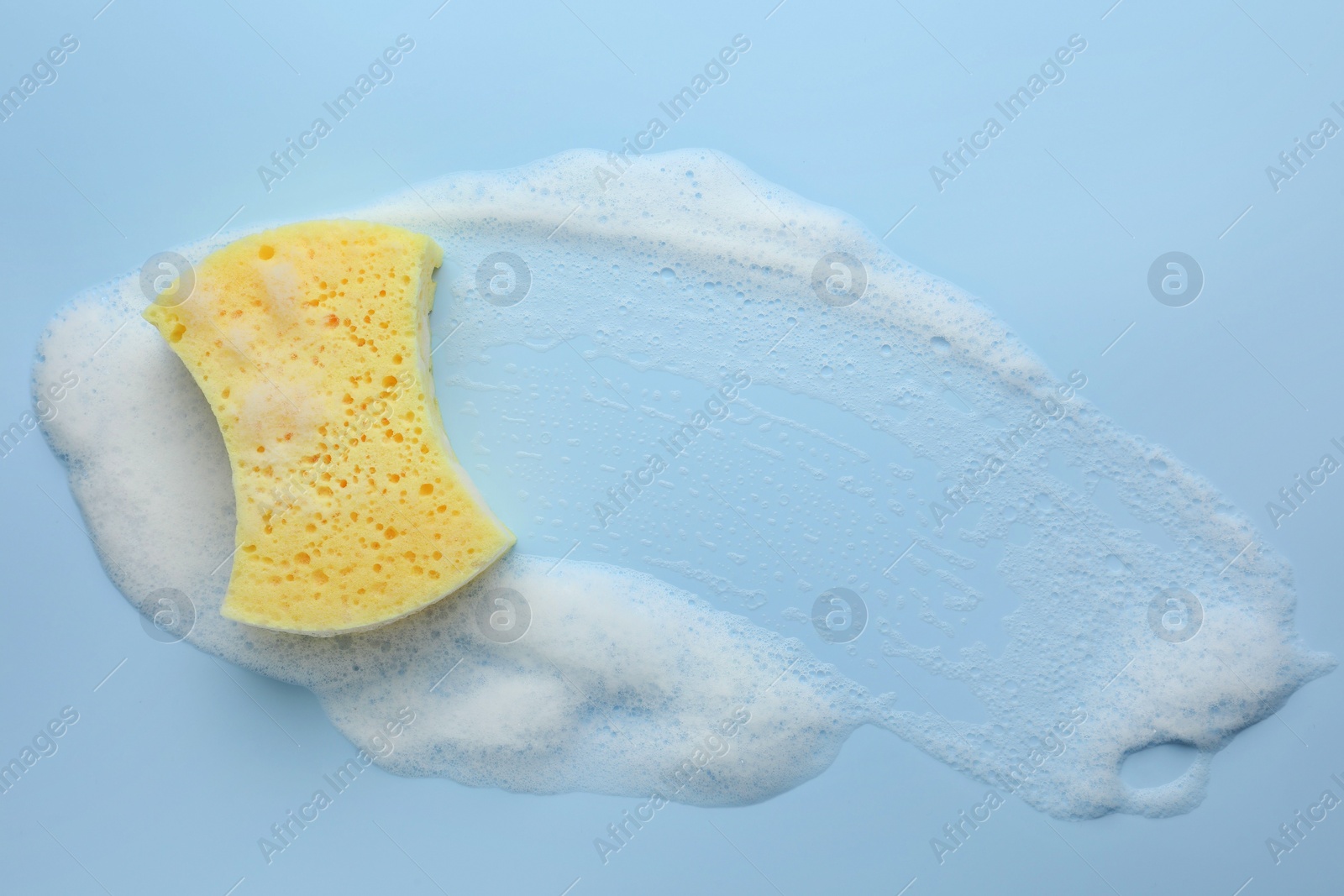 Photo of Yellow sponge with foam on light blue background, top view.