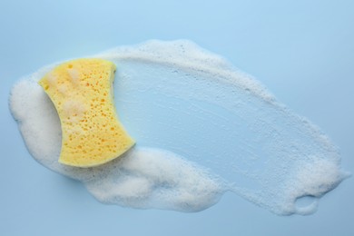 Yellow sponge with foam on light blue background, top view.