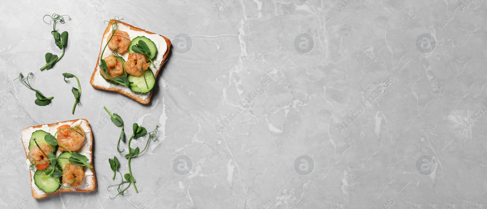 Image of Tasty toasts with cream cheese, shrimps, cucumbers and microgreens on grey marble table, flat lay with space for text. Banner design