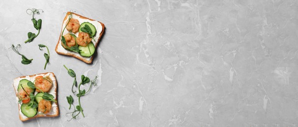 Image of Tasty toasts with cream cheese, shrimps, cucumbers and microgreens on grey marble table, flat lay with space for text. Banner design