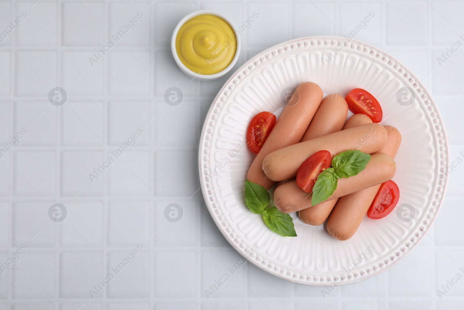 Photo of Delicious boiled sausages with tomatoes, basil and sauce on white tiled table, top view. Space for text