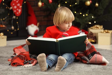 Photo of Little child reading book on floor at home. Christmas celebration