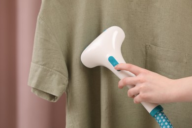 Photo of Woman steaming T-shirt on light background, closeup