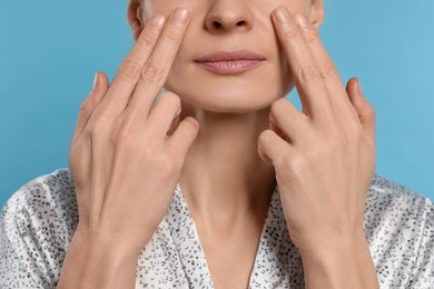 Photo of Woman massaging her face on turquoise background, closeup