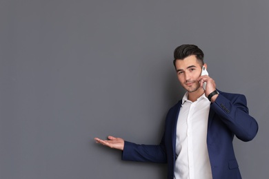 Handsome young man talking on phone against grey background. Space for text