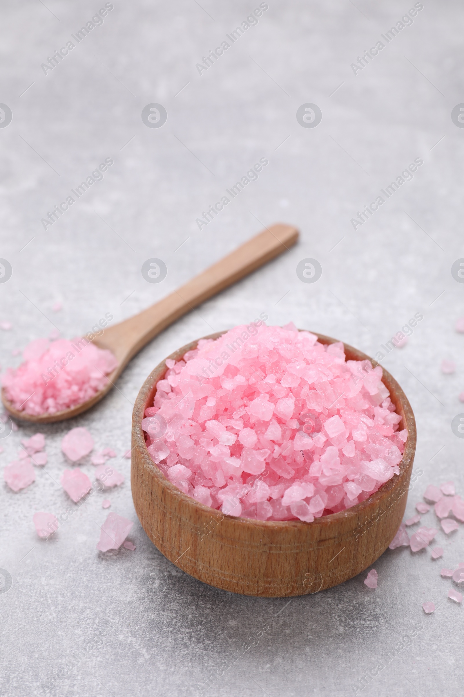 Photo of Bowl and spoon with pink sea salt on light grey table, space for text