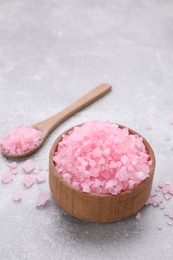 Photo of Bowl and spoon with pink sea salt on light grey table, space for text