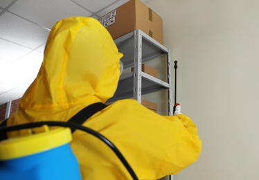 Photo of Pest control worker spraying pesticide on rack indoors