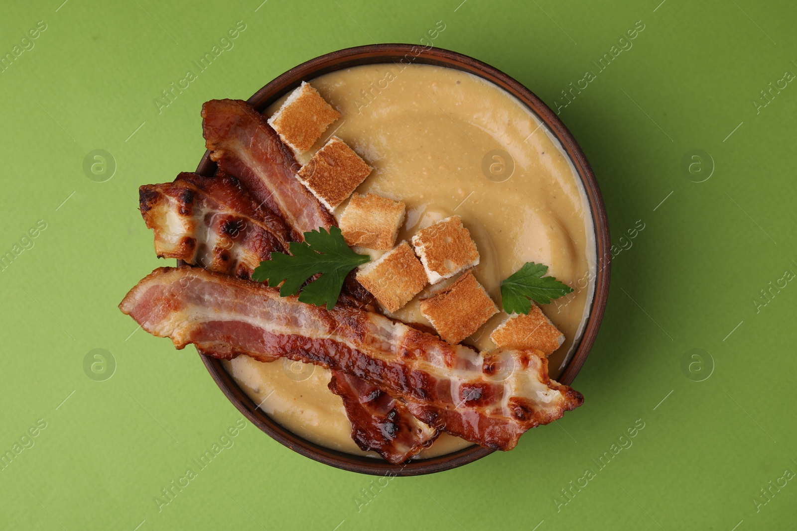 Photo of Delicious lentil soup with bacon and parsley in bowl on green table, top view