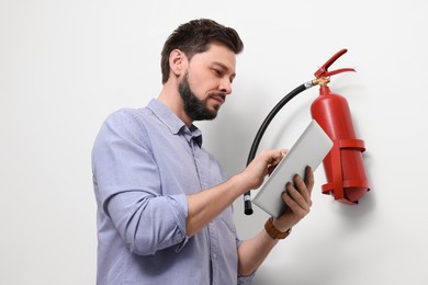 Photo of Man with tablet checking fire extinguisher indoors