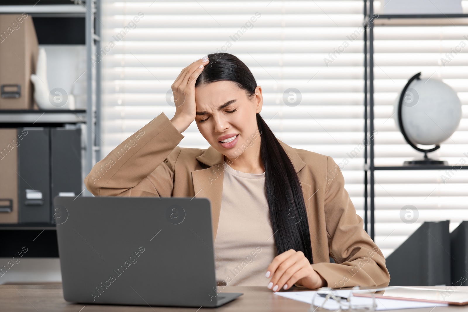 Photo of Woman suffering from headache at workplace in office