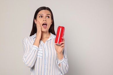 Emotional young woman holding tin can with beverage on light grey background. Space for text