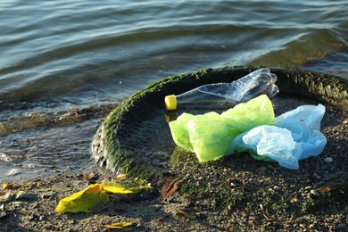 Photo of Plastic trash and tire on sand near water. Environment pollution