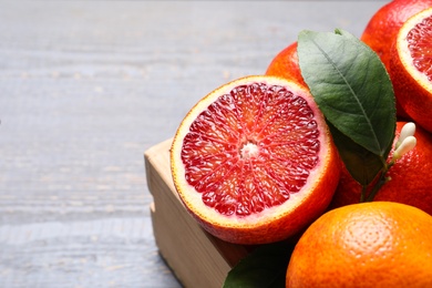 Ripe red oranges in crate on grey wooden table, closeup. Space for text