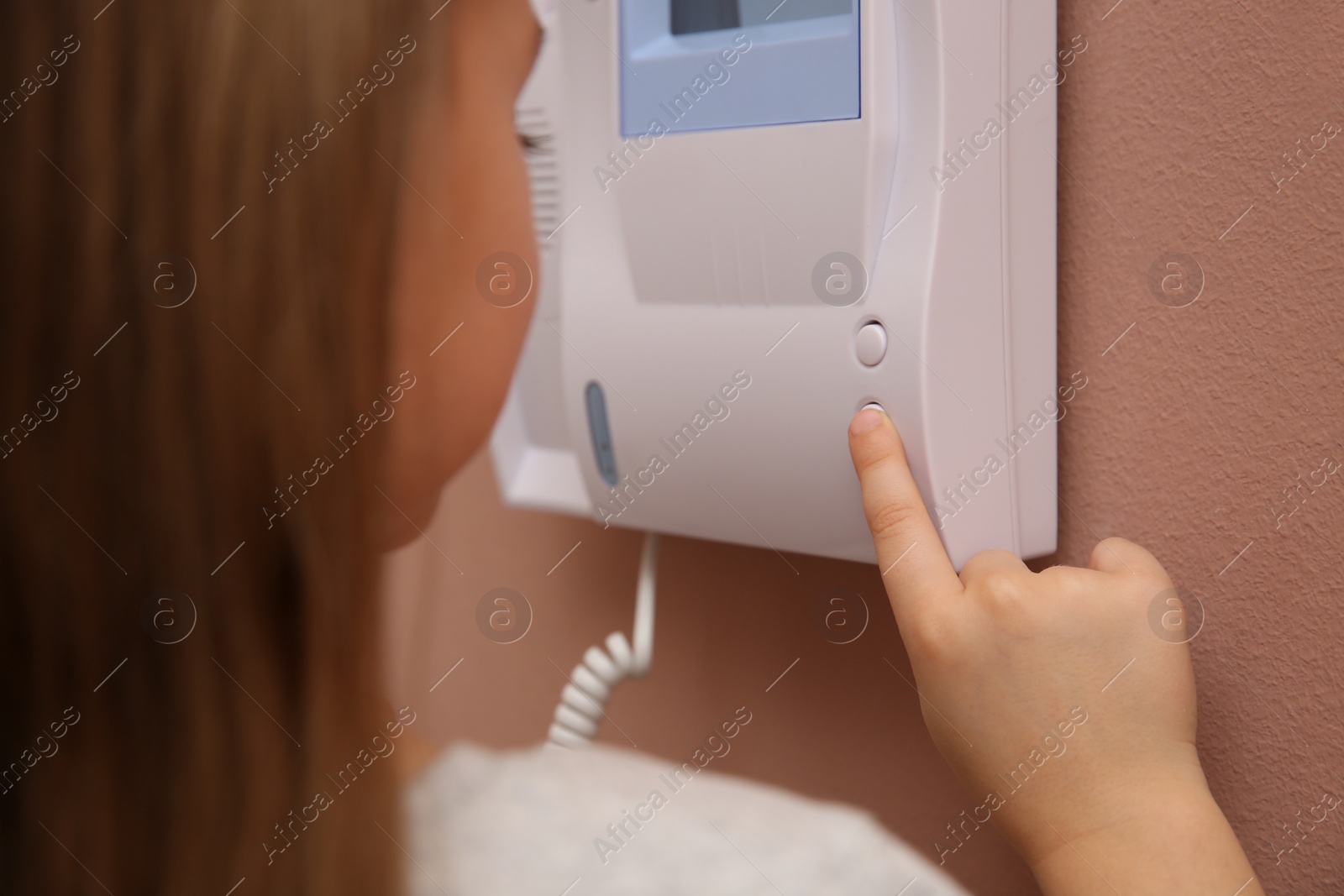 Photo of Cute little girl answering intercom call indoors, closeup